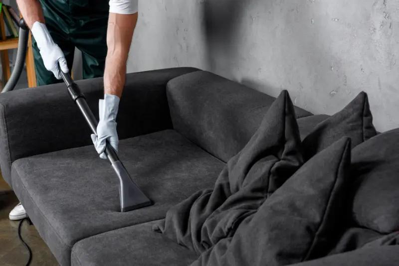 L'homme utilise un aspirateur pour nettoyer un canapé.