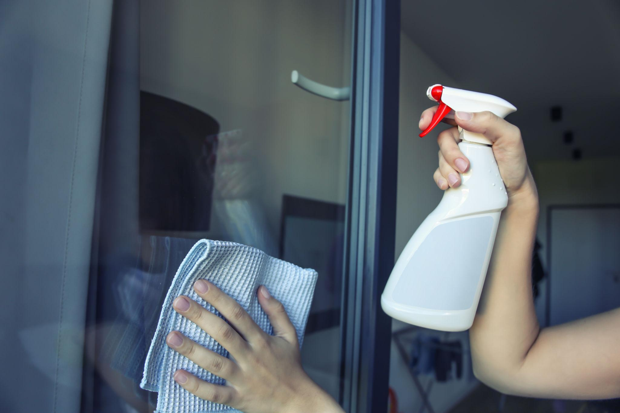 L'employé nettoie les vitres d'une porte vitrée avec un chiffon et un spray de nettoyage.
